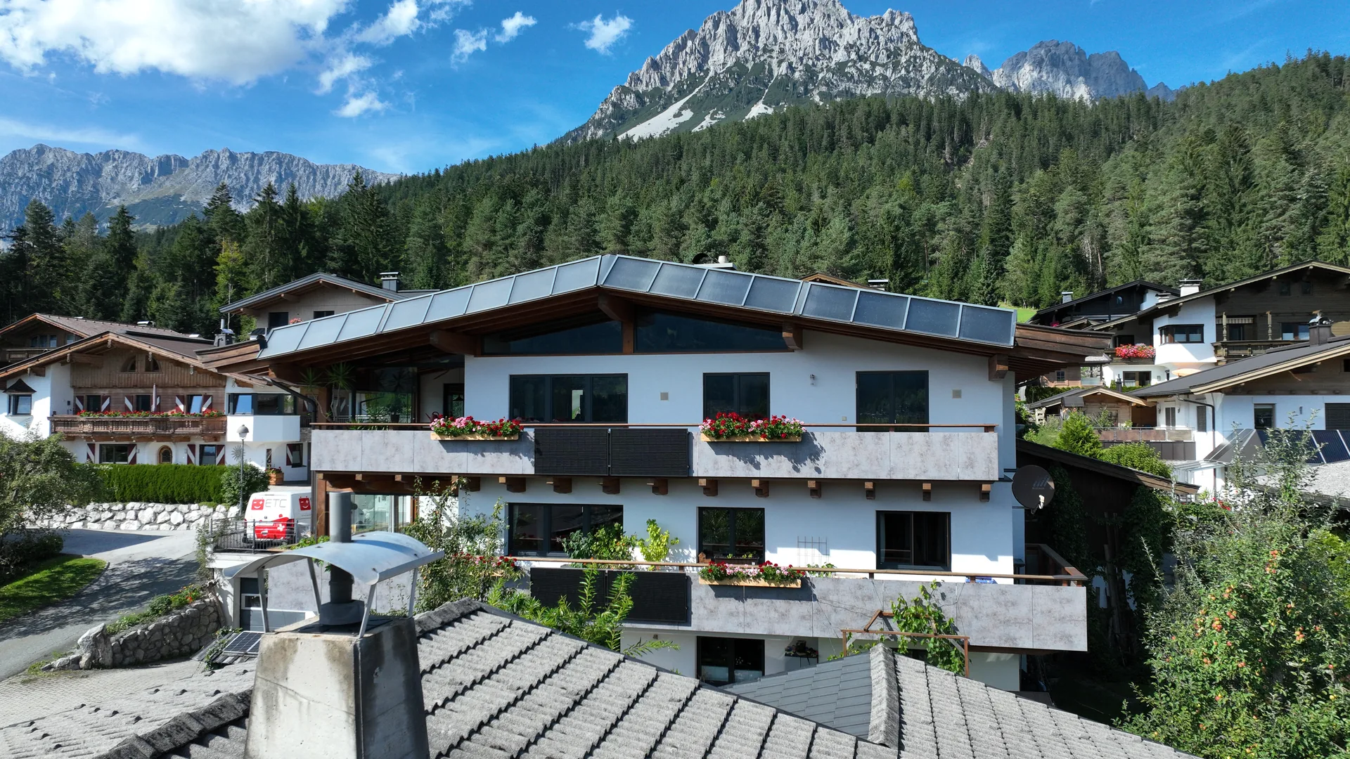 Außenansicht des FALKENSITZ Apartment-Hauses in Ellmau mit Solarpaneelen und Blumenkästen
